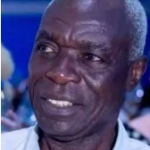 Retrato em grande plano de Vicy António, antiga glória do futebol angolano. É um homem negro de idade avançada, com cabelo curto grisalho e expressão serena mas resiliente. Ele veste uma camisa clara e olha ligeiramente para o lado com um meio sorriso.